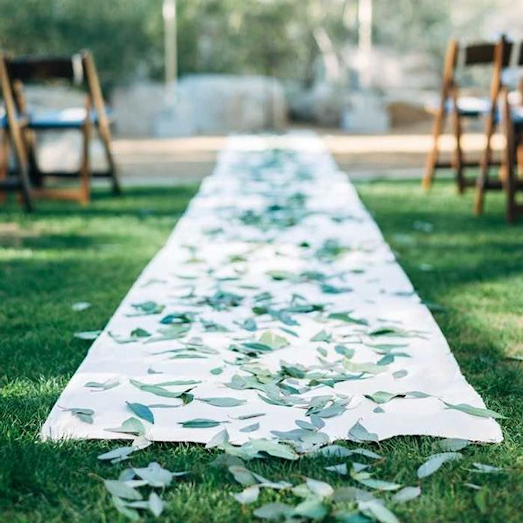 Fresh-cut eucalyptus leaves lining a wedding aisle as a natural runner alternative